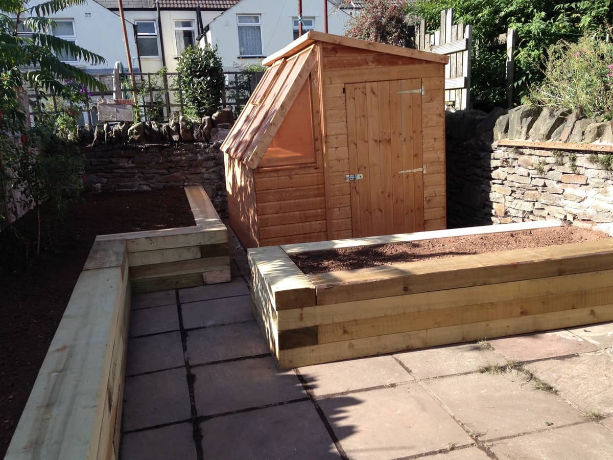 Cathays: oak sleeper raised beds and stone walling behind a timber workshop.