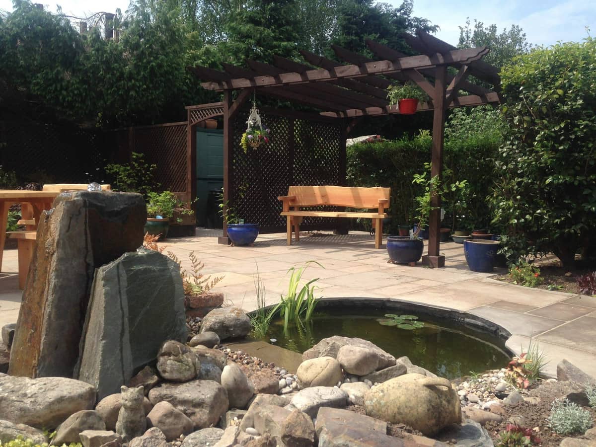 A pergola walk beside a wildlife pond with a slate water feature.
