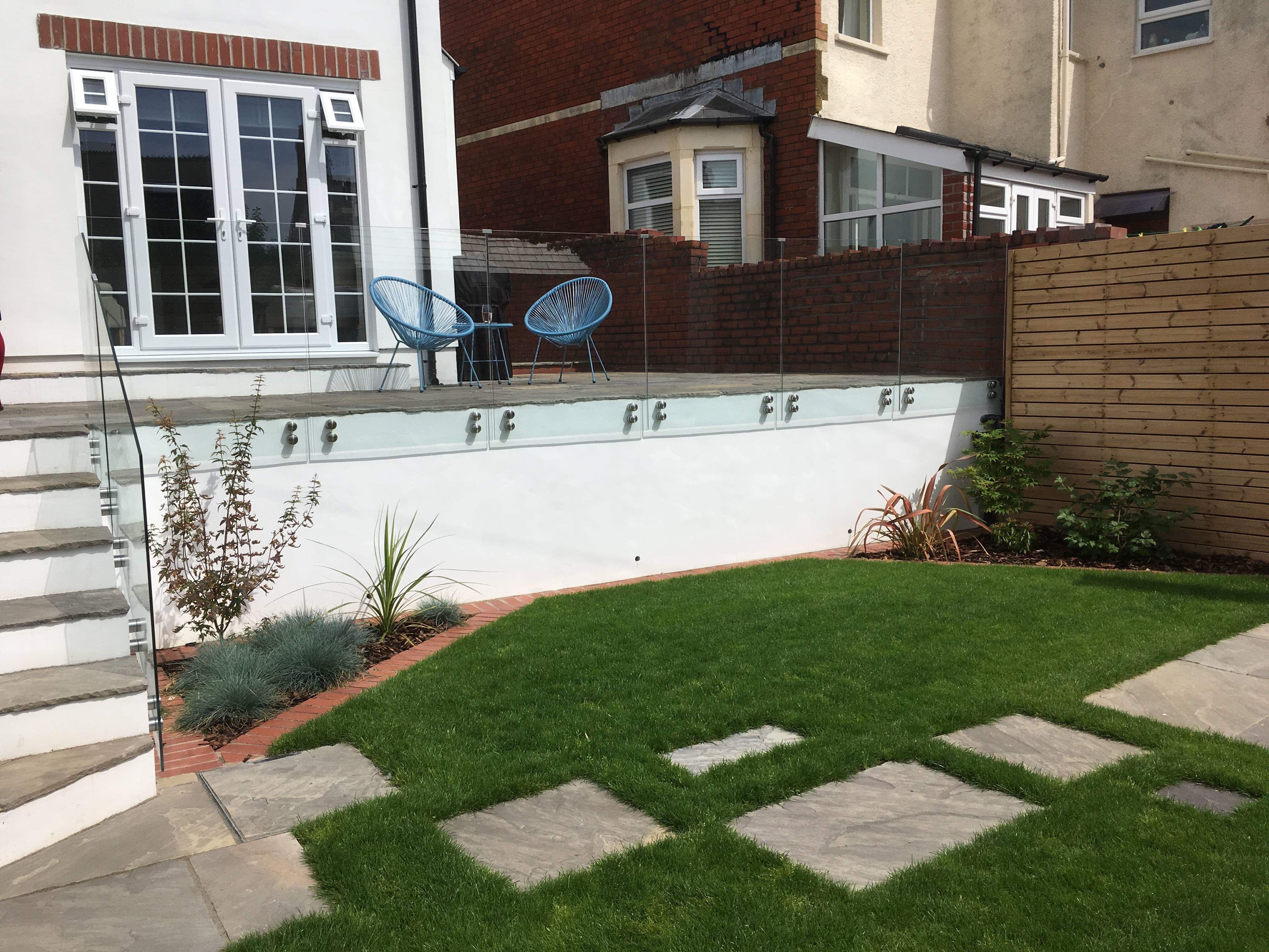 Modern domestic back garden with new lawn, stepping stones, white walls and timber-clad fence
